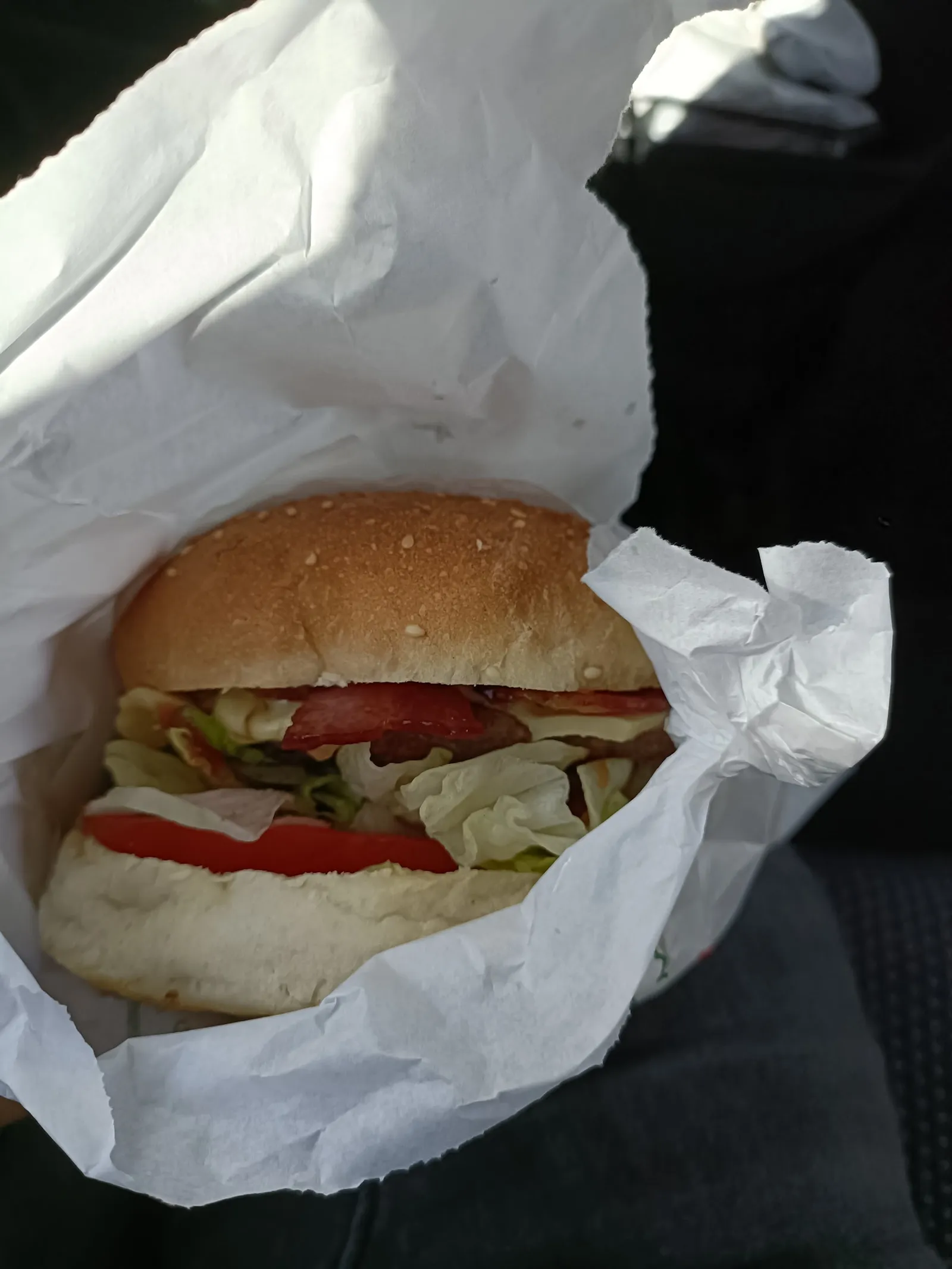 Burger in a white paper bag held by a customer in a car