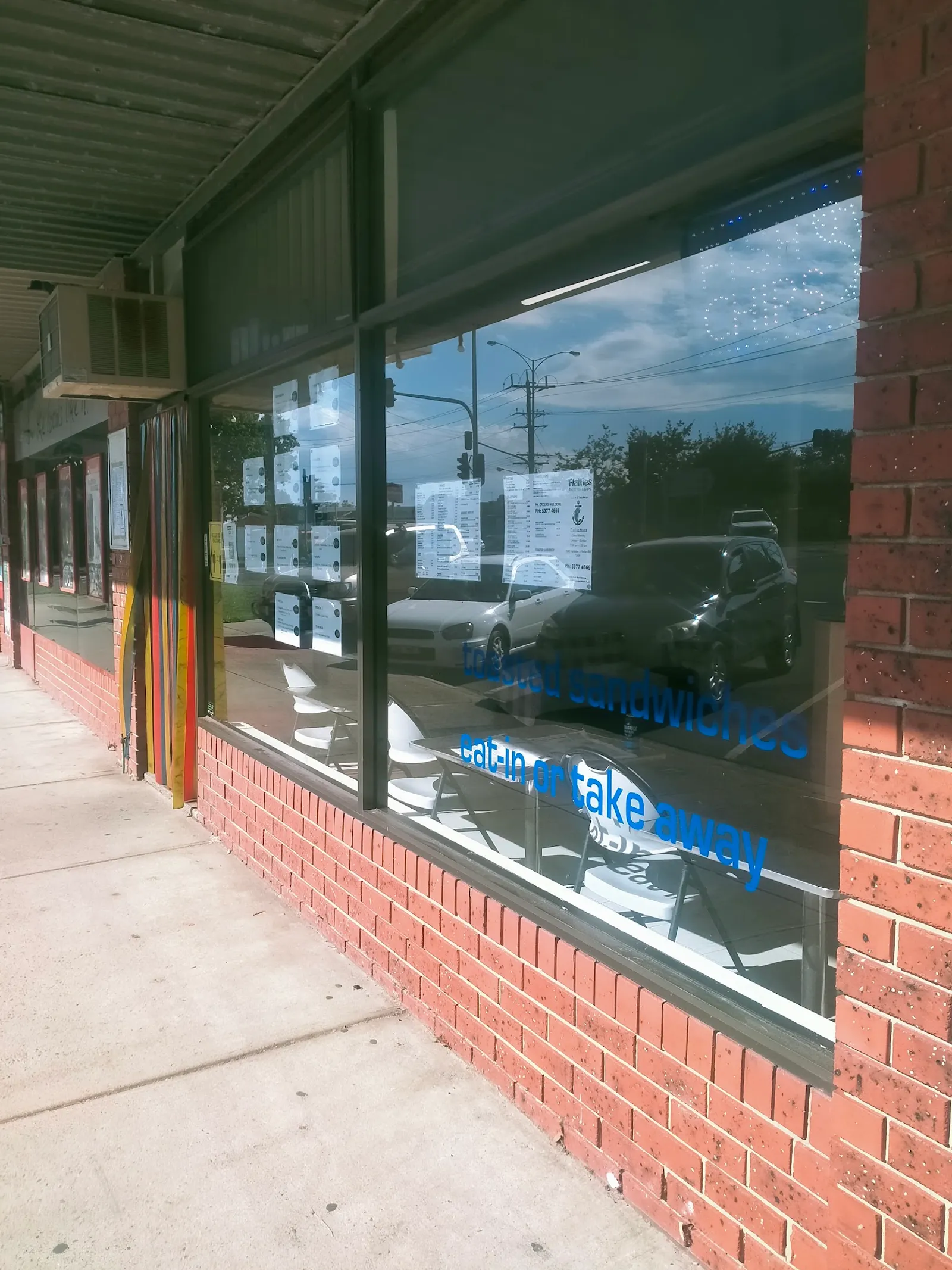 Side-angle view of Flatties shopfront window with 'eat in or takeaway' vinyl lettering