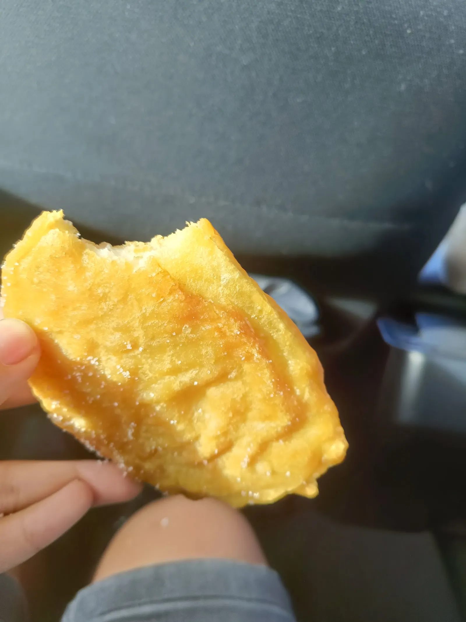 Half-eaten piece of battered fish held by a hand in a car