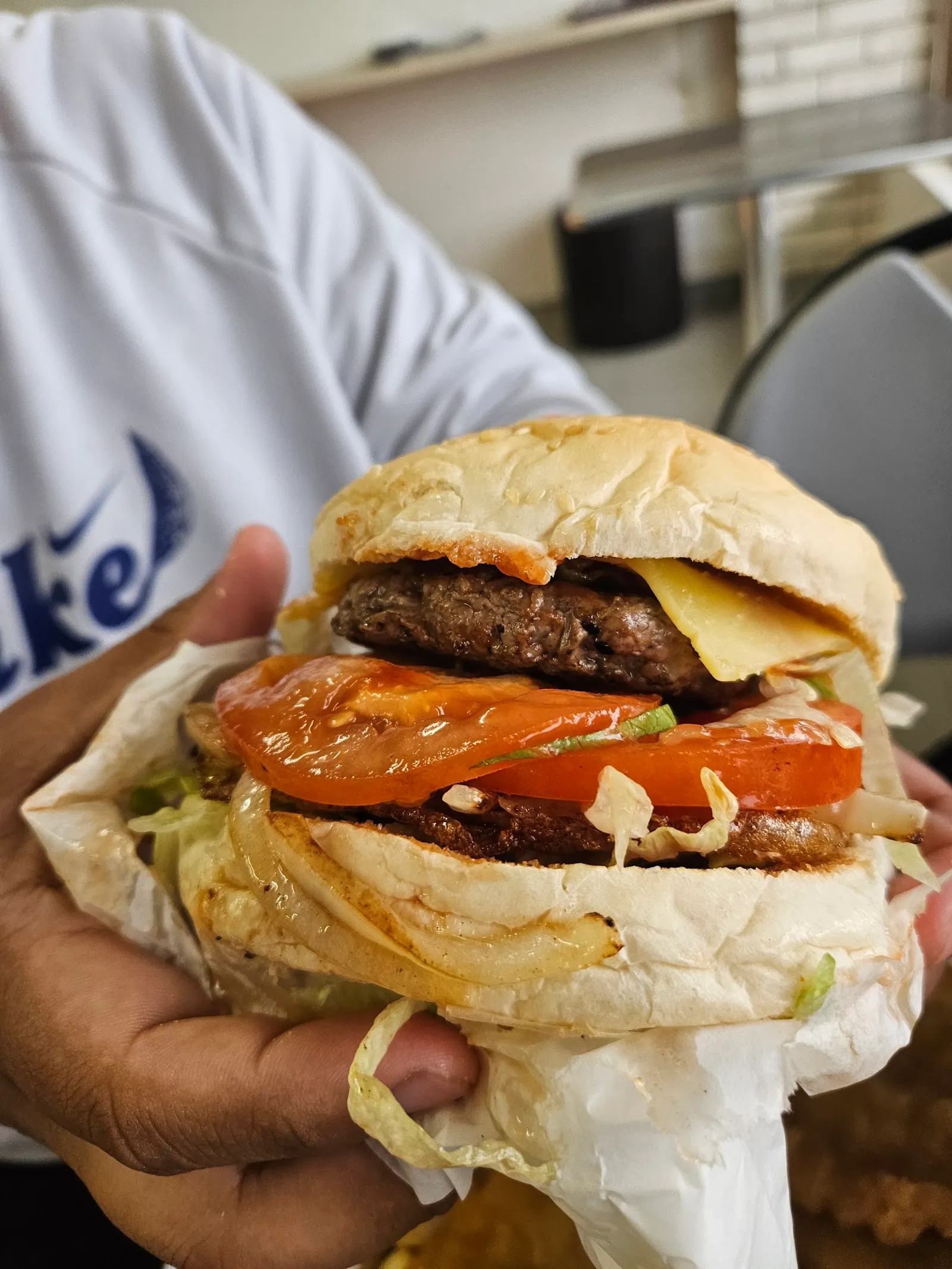 Hands holding a large loaded burger with beef, cheese, tomato and salad inside the shop