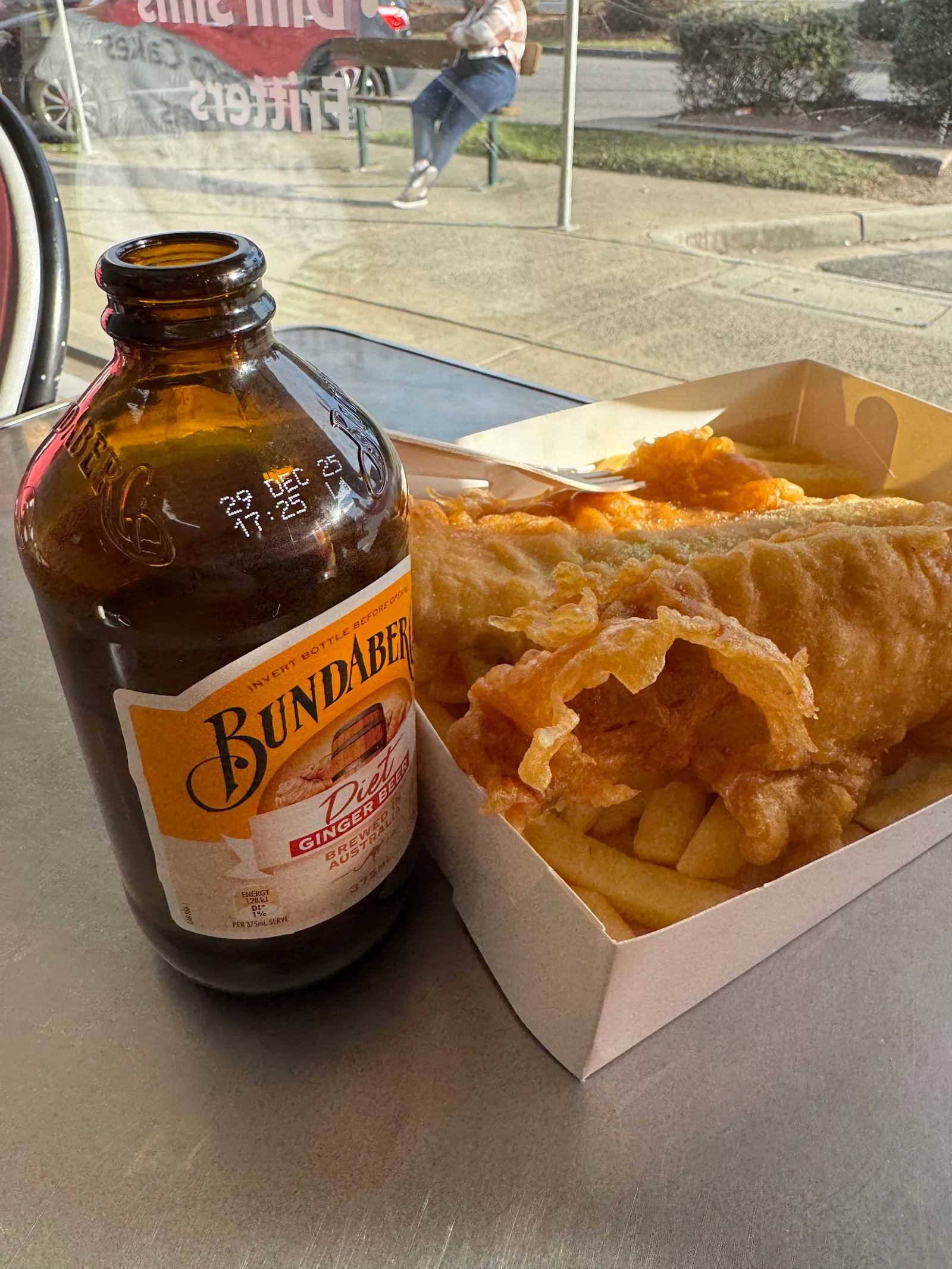 Bundaberg ginger beer bottle next to a box of fish and chips on an outdoor counter